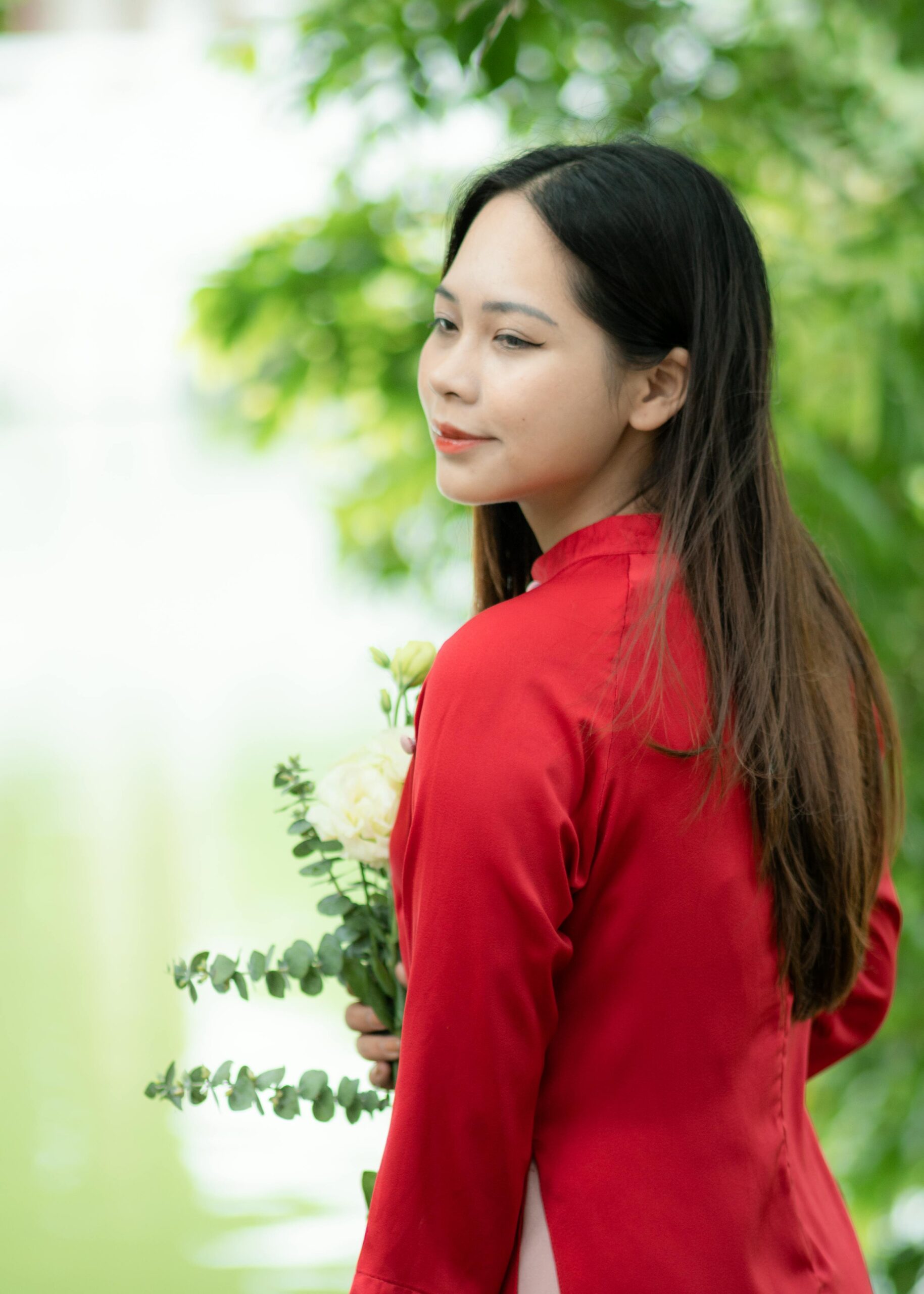Portrait of an East Asian woman in a red áo dài, outdoors in Vietnam.