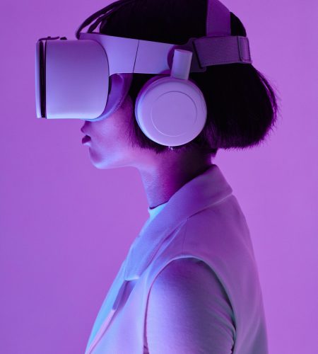 Side profile of a woman wearing VR goggles in a studio with purple lighting, embodying future tech.