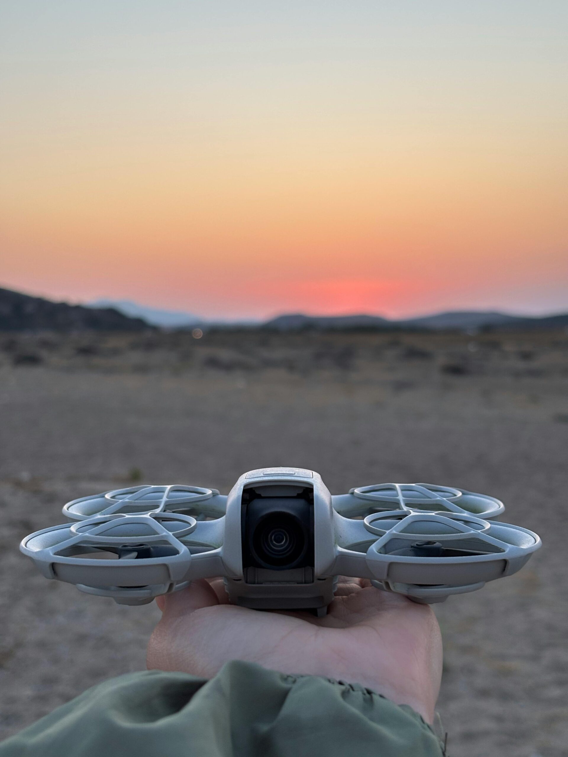 Silhouette of a drone held against a vivid sunset in a desert landscape.